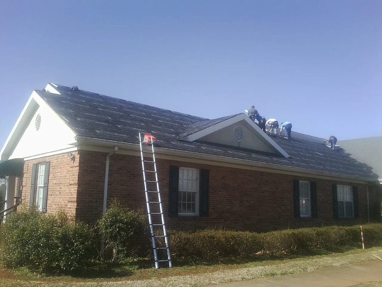 Crew tearing shingles off a brick ranch roof with a ladder set — Emergency Roof Repair work by our crew in Hull